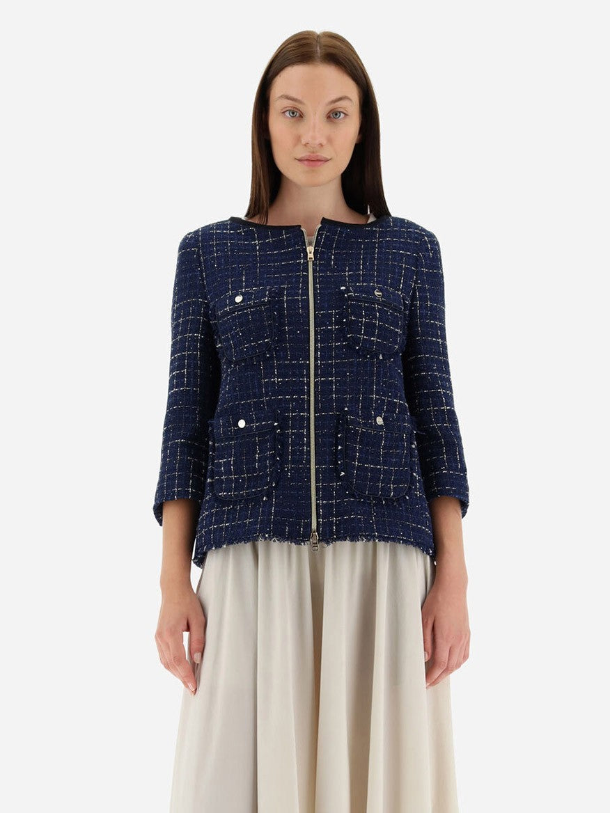 A woman stands wearing a Herno Jacket in Casual Tweed in New Blue, complete with practical pockets, paired with a cream skirt against a plain background.