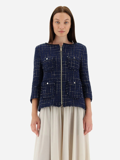 A woman stands wearing a Herno Jacket in Casual Tweed in New Blue, complete with practical pockets, paired with a cream skirt against a plain background.