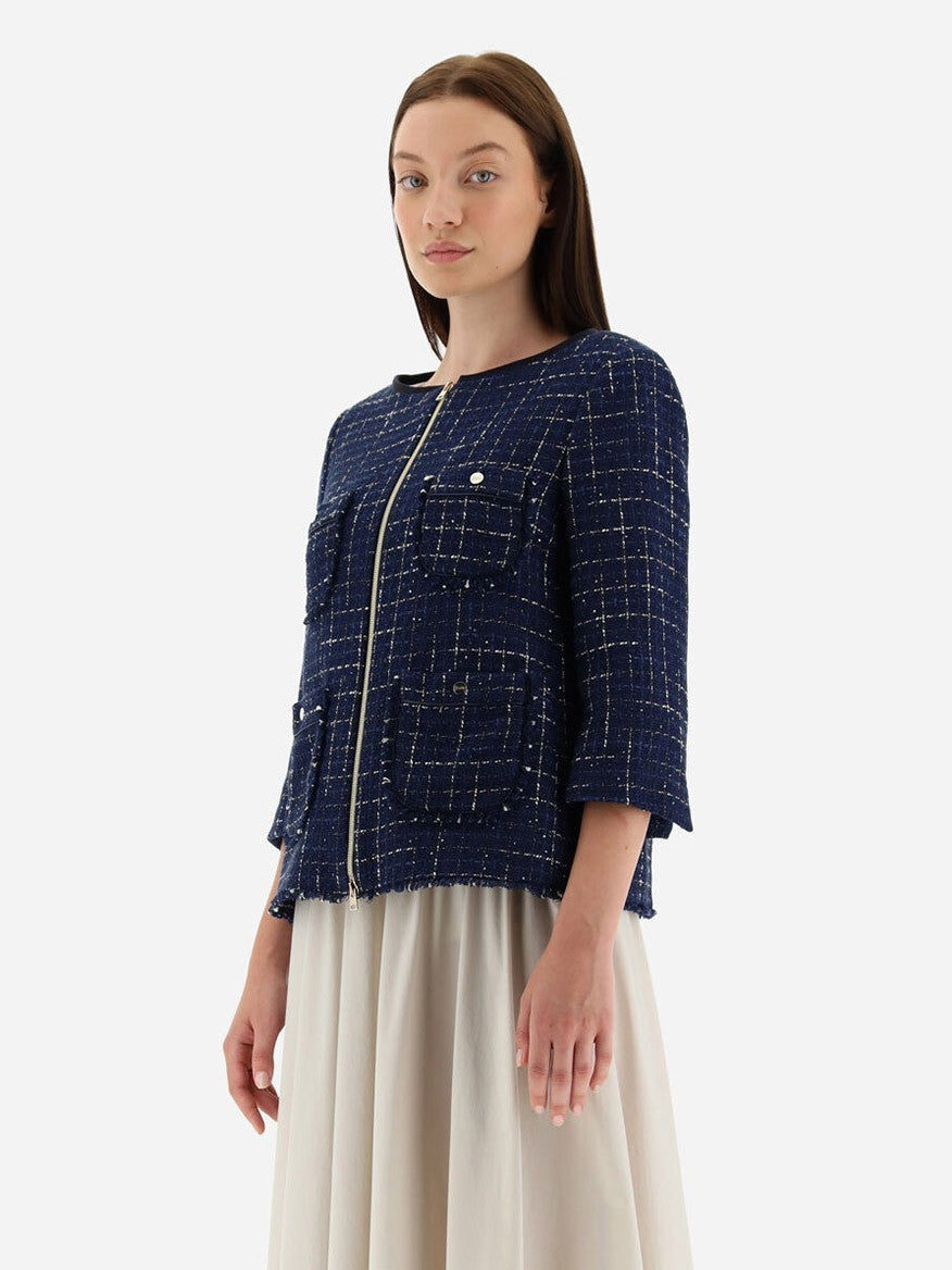 Against a plain white background, a woman poses gracefully in a Herno Jacket in Casual Tweed in New Blue adorned with lurex and sequins, complete with front pockets. Her light-colored skirt elegantly complements her look.