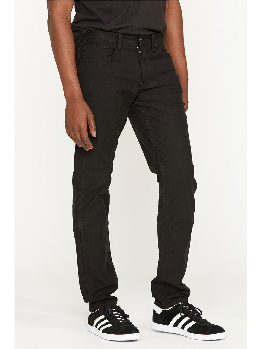 A person standing in Hudson Blake Slim Straight Twill Pant in Black and sneakers.