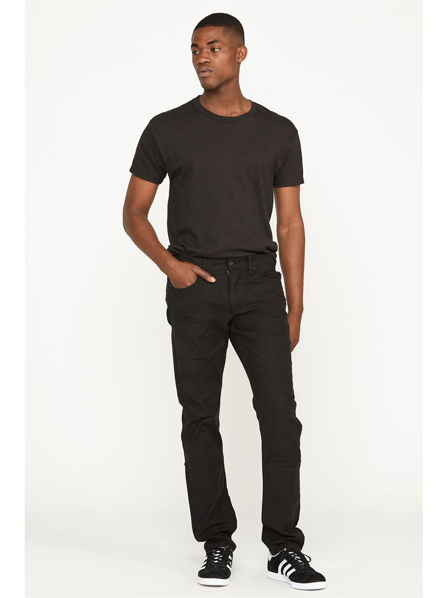 Man standing in a relaxed pose wearing a black t-shirt, Hudson Blake Slim Straight Twill Pant in Black, and black sneakers.