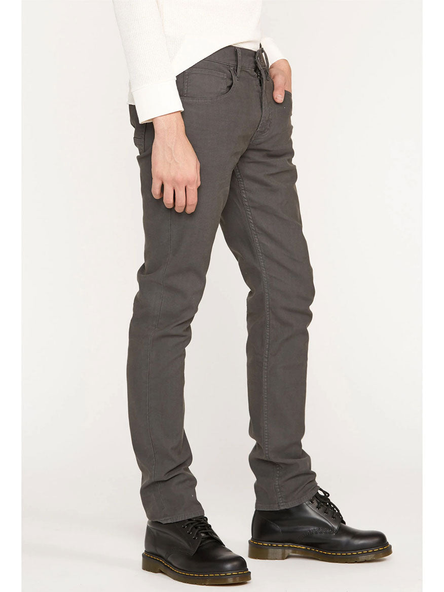 A person wearing Hudson Blake Slim Straight Twill Jean in Dark Grey and black shoes.