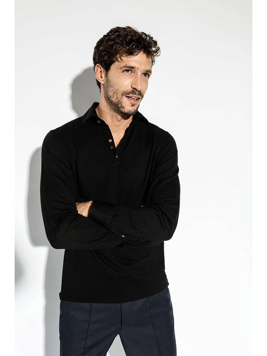 Man with wavy hair wearing an Isaia Evening Polo in Black and dark pants, standing against a white background, with arms crossed.