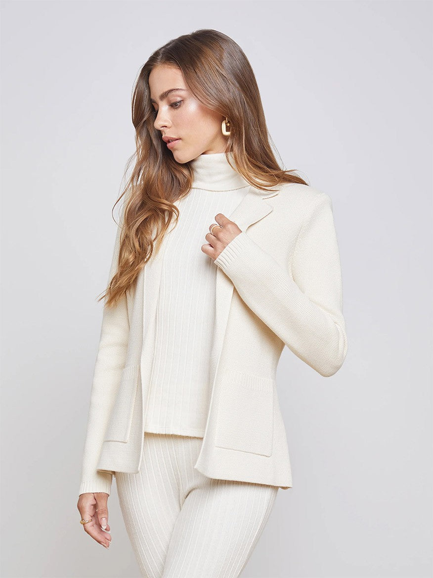 A woman in a chic L'Agence Lacey Knit Blazer in Porcelain beige turtleneck and matching pants posing against a grey background.
