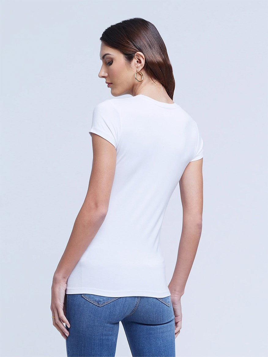 A woman standing sideways, wearing the L'Agence Ressi Short Sleeve Crew in White and blue jeans, made in the USA.