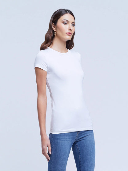 A woman wearing a L'Agence Ressi Short Sleeve Crew in White and blue jeans standing against a plain background.