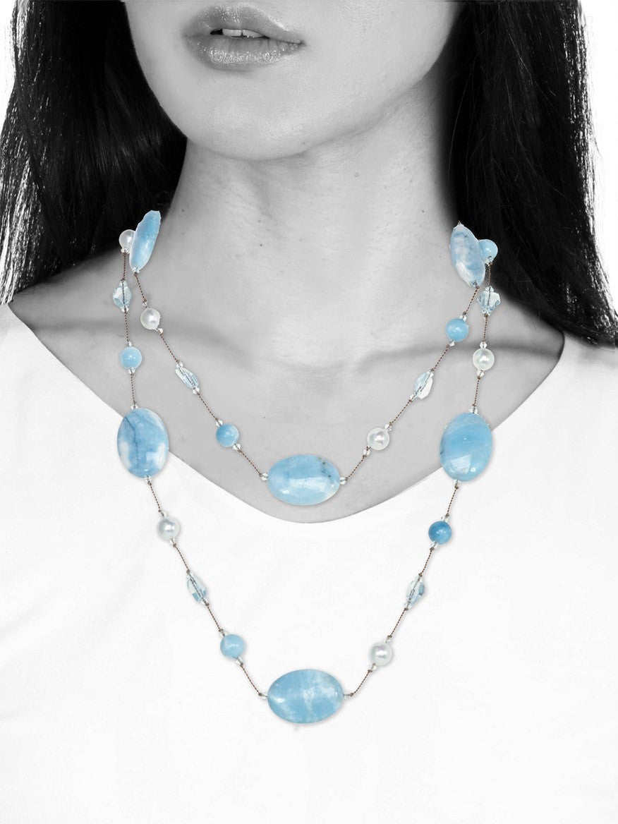 A black and white image of a woman wearing a Margo Morrison Oval Blue Larimar Necklace with Blue Topaz, with the necklace being the only item in color.