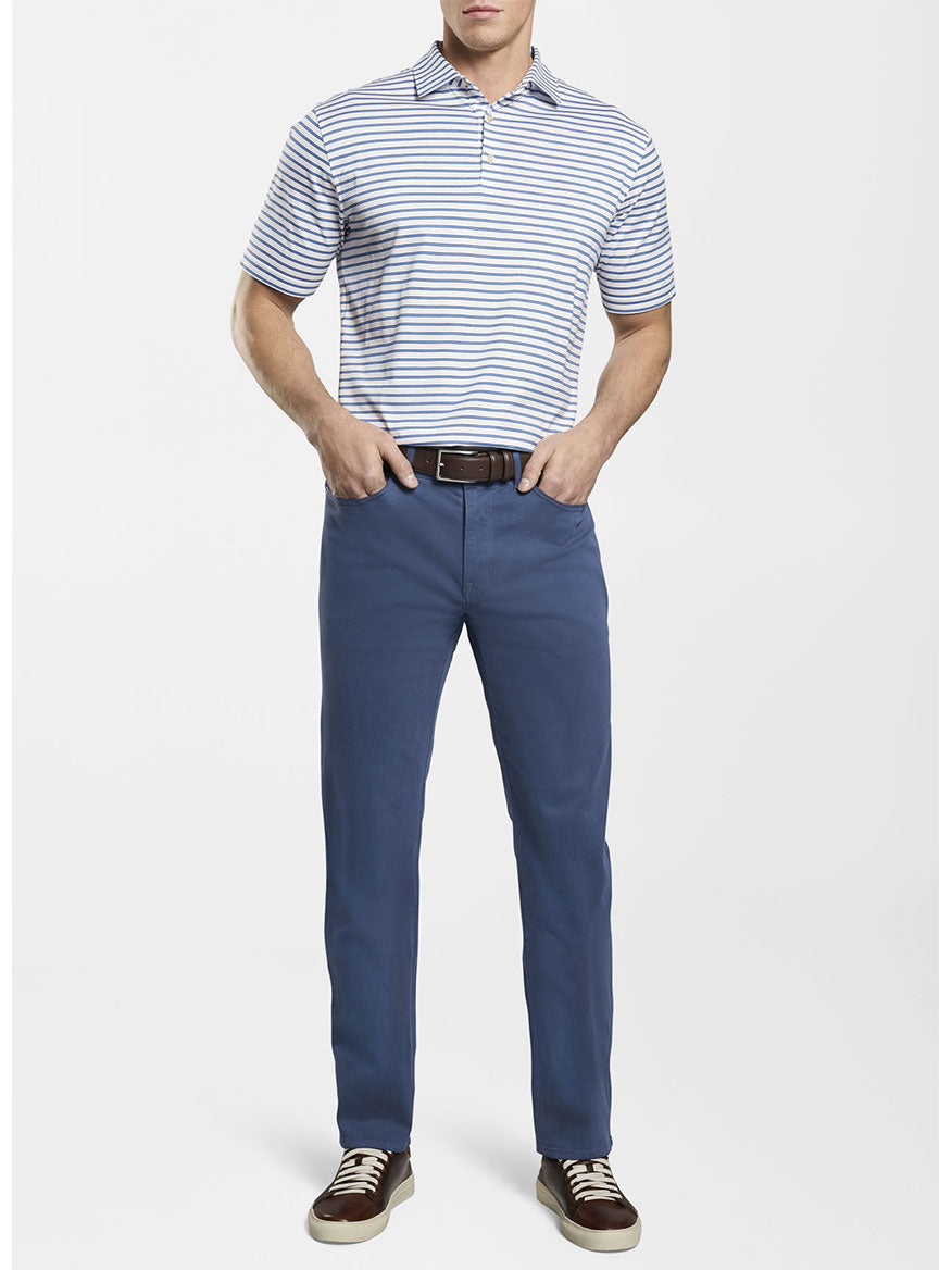 A man wearing a classic fit blue striped polo shirt and Peter Millar Ultimate Sateen Five-Pocket Pant in Navy.