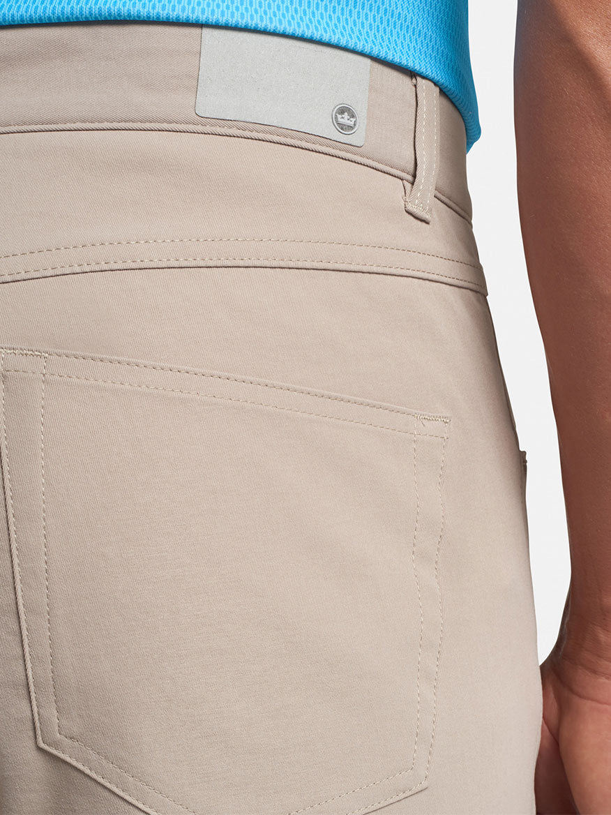 Close-up of a person wearing Peter Millar Performance Five-Pocket Pant in Khaki with a blue shirt tucked in, focusing on the pocket detail and a visible portion of a belt.