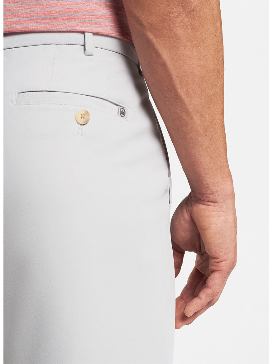 Close-up view of a person's side waist and hip area wearing light gray Peter Millar Salem High Drape Performance Shorts with a buttoned pocket detail in British Grey.