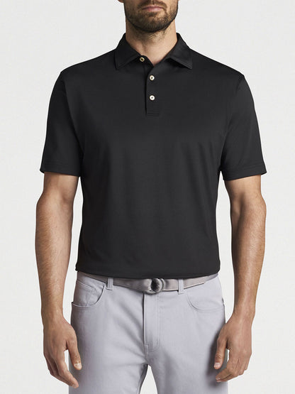 A man wearing a Peter Millar Solid Performance Jersey Polo in Black and grey pants made of moisture-wicking fabric.