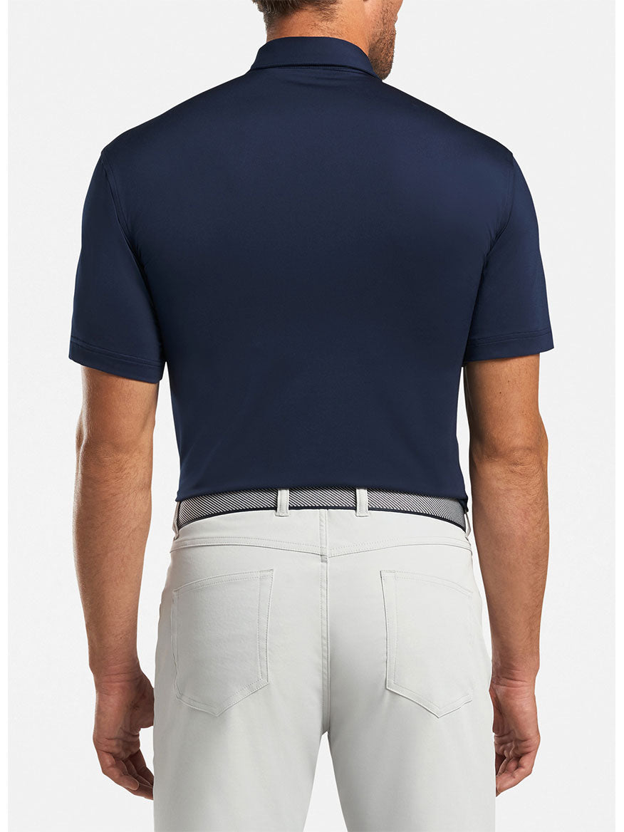 The back view of a man wearing a Peter Millar Solid Performance Jersey Polo in Navy and white pants.