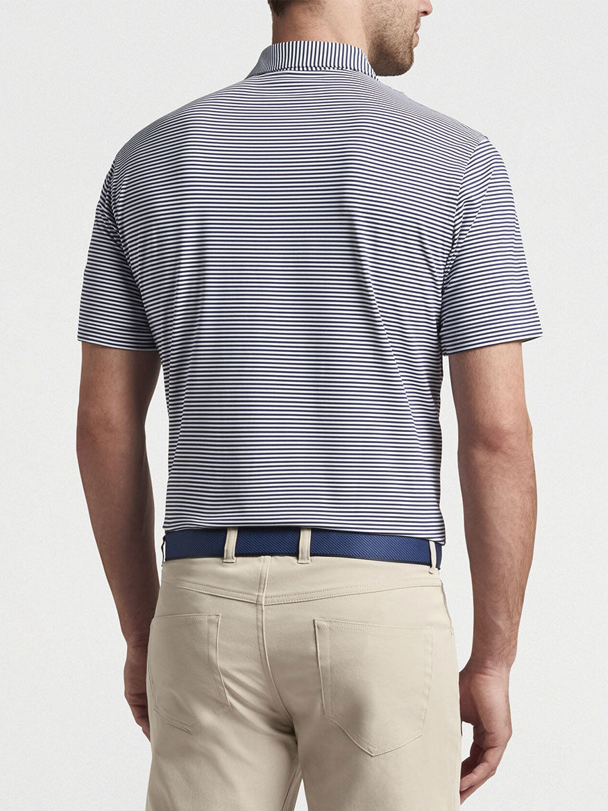 Man wearing a Peter Millar Hales Performance Jersey Polo in Navy and beige pants with a blue belt, viewed from behind.