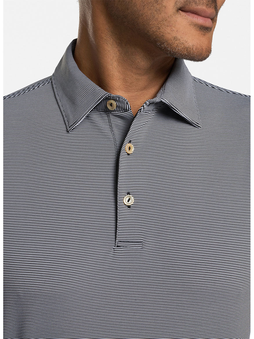 Man wearing a Peter Millar Jubilee Stripe Performance Polo in black, a moisture-wicking shirt with gray and black stripes and three buttons, slight smile visible.