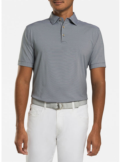 A person is wearing a black Peter Millar Jubilee Stripe Performance Polo with white pants and a gray belt, standing against a plain background.