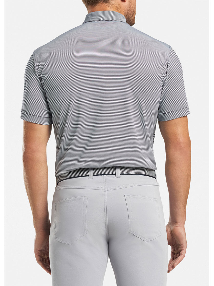 The back view of a man wearing grey pants and a Peter Millar Jubilee Stripe Performance Polo in Navy.