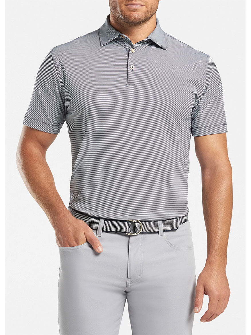 A man wearing a Peter Millar Jubilee Stripe Performance Polo in Navy and gray pants that provides UPF 50+ sun protection.