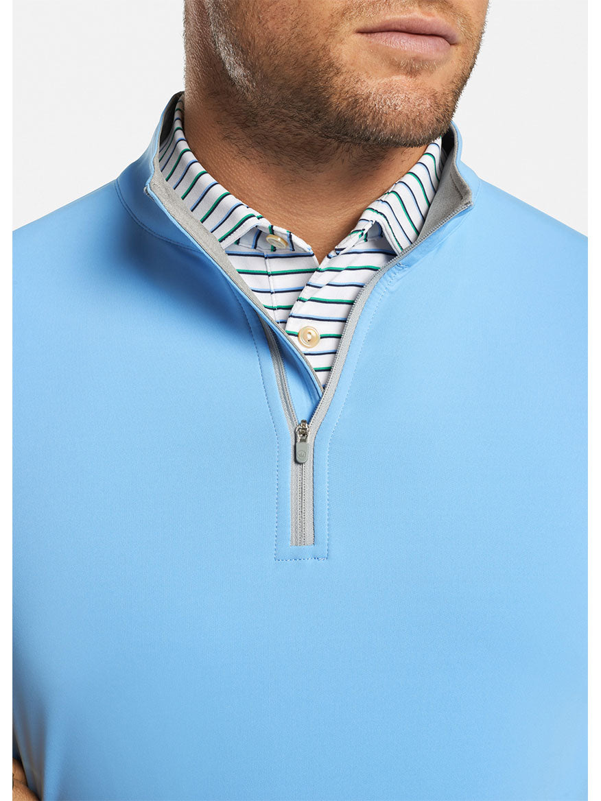 Man wearing a blue Peter Millar Perth Performance Quarter-Zip in Cottage Blue over a striped collared shirt.