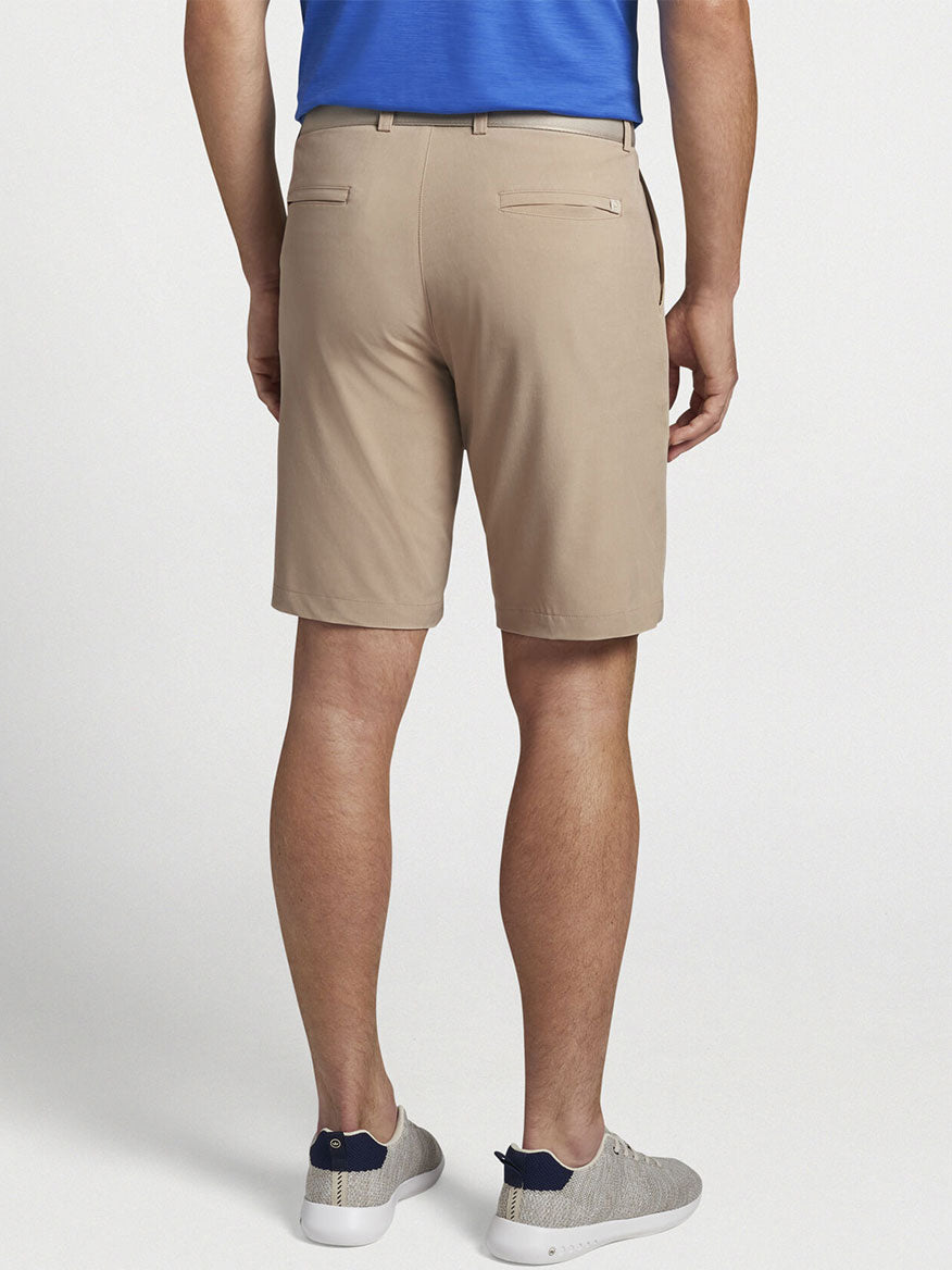 The back view of a man wearing Peter Millar Shackleford Performance Hybrid Short in Beech Wood polo shirt and shorts.