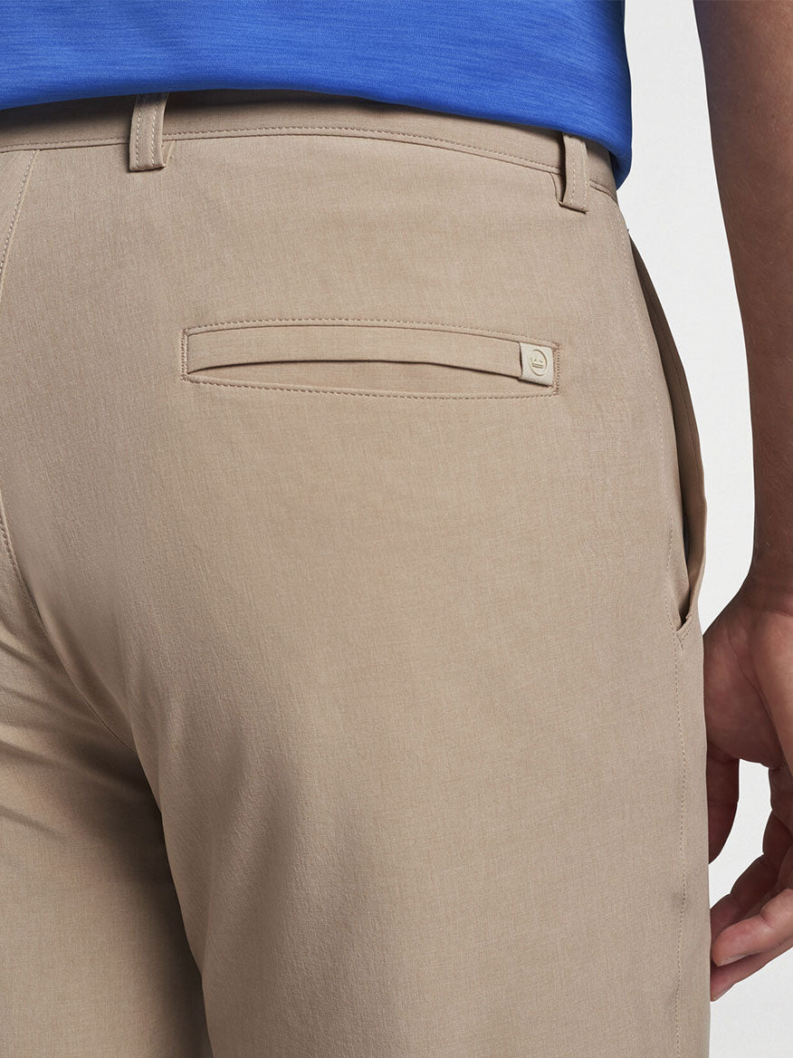 The back view of a man wearing the Peter Millar Shackleford Performance Hybrid Short in Beech Wood, made from water-resistant performance fabric with four-way stretch.