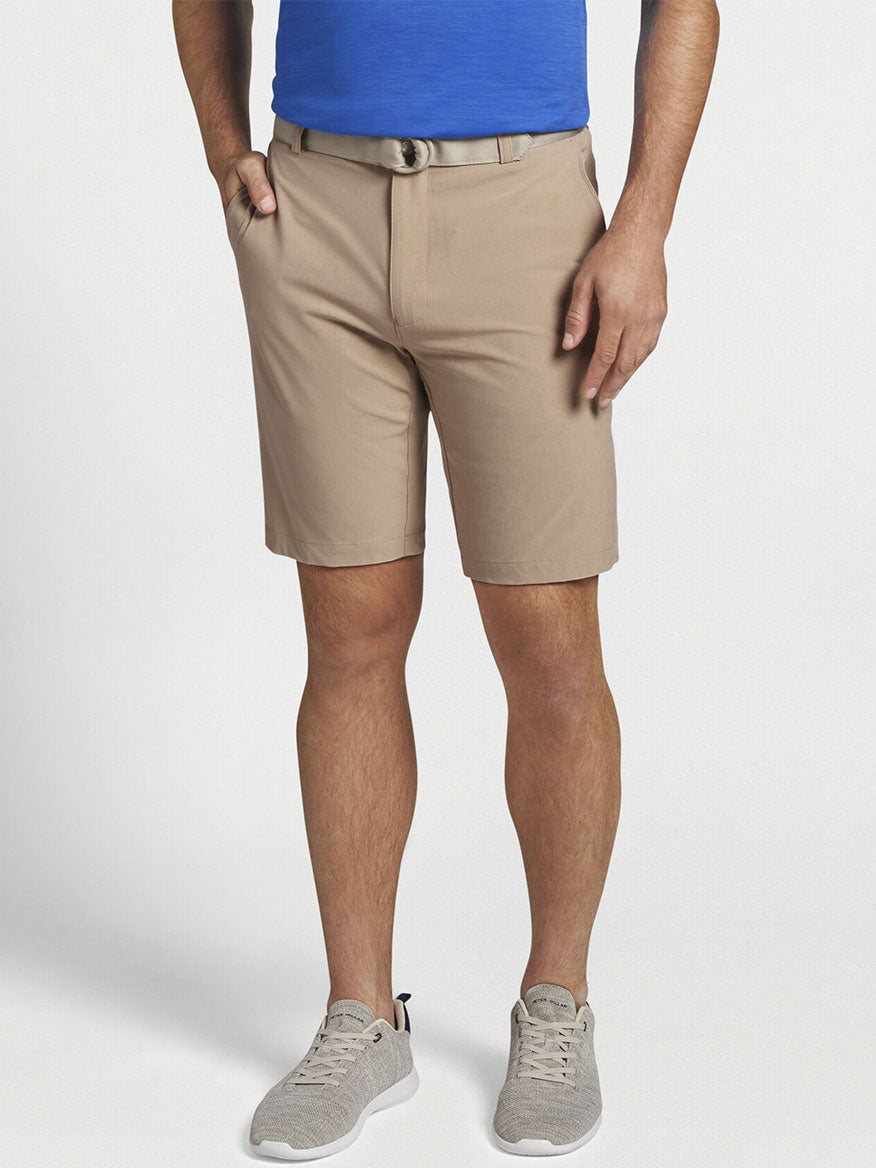 A versatile man dressed in a blue shirt and Peter Millar Shackleford Performance Hybrid Short in Beech Wood made with water-resistant performance fabric for maximum comfort and four-way stretch capabilities.