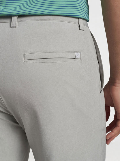 The back view of a man wearing a grey polo shirt and Peter Millar Shackleford Performance Hybrid Short in British Grey made of versatile performance fabric.