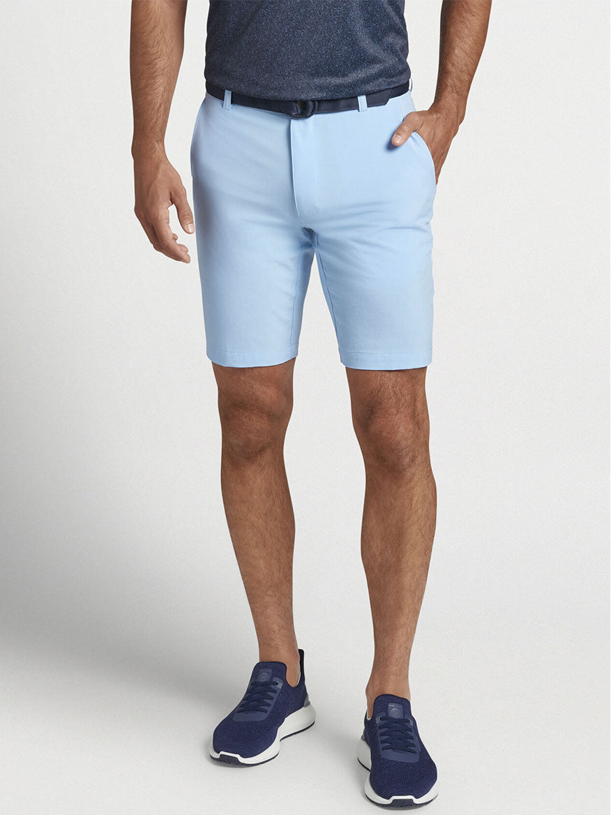 A man wearing the Peter Millar Shackleford Performance Hybrid Short in Cottage Blue and a blue shirt made of versatile performance fabric for enhanced mobility.