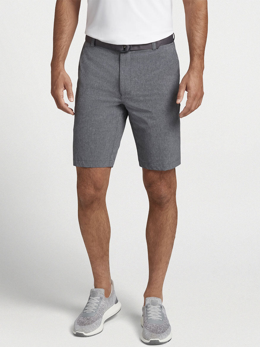 A versatile man wearing the Peter Millar Shackleford Performance Hybrid Short in Iron with a 10" inseam, made from performance fabric, paired with a white shirt.