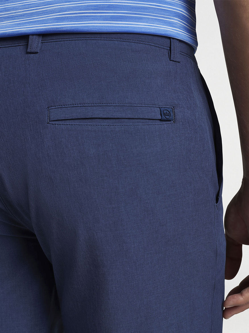 The back view of a man wearing a blue polo shirt and Peter Millar Shackleford Performance Hybrid Short in Navy.