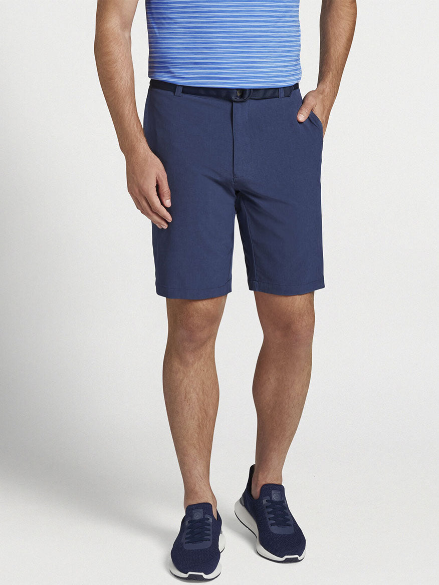 The man is wearing a blue striped shirt and Peter Millar Shackleford Performance Hybrid Short in Navy, making his outfit a versatile essential for any course or swim trunks.