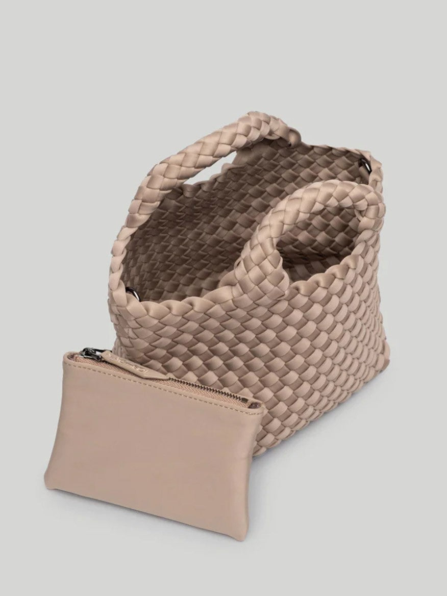 The Naghedi St. Barths Petit Tote in Solid Cashmere, a beige woven handbag with a handle, is displayed alongside a matching beige zippered pouch on a plain background, featuring a convenient crossbody strap for versatile wear.
