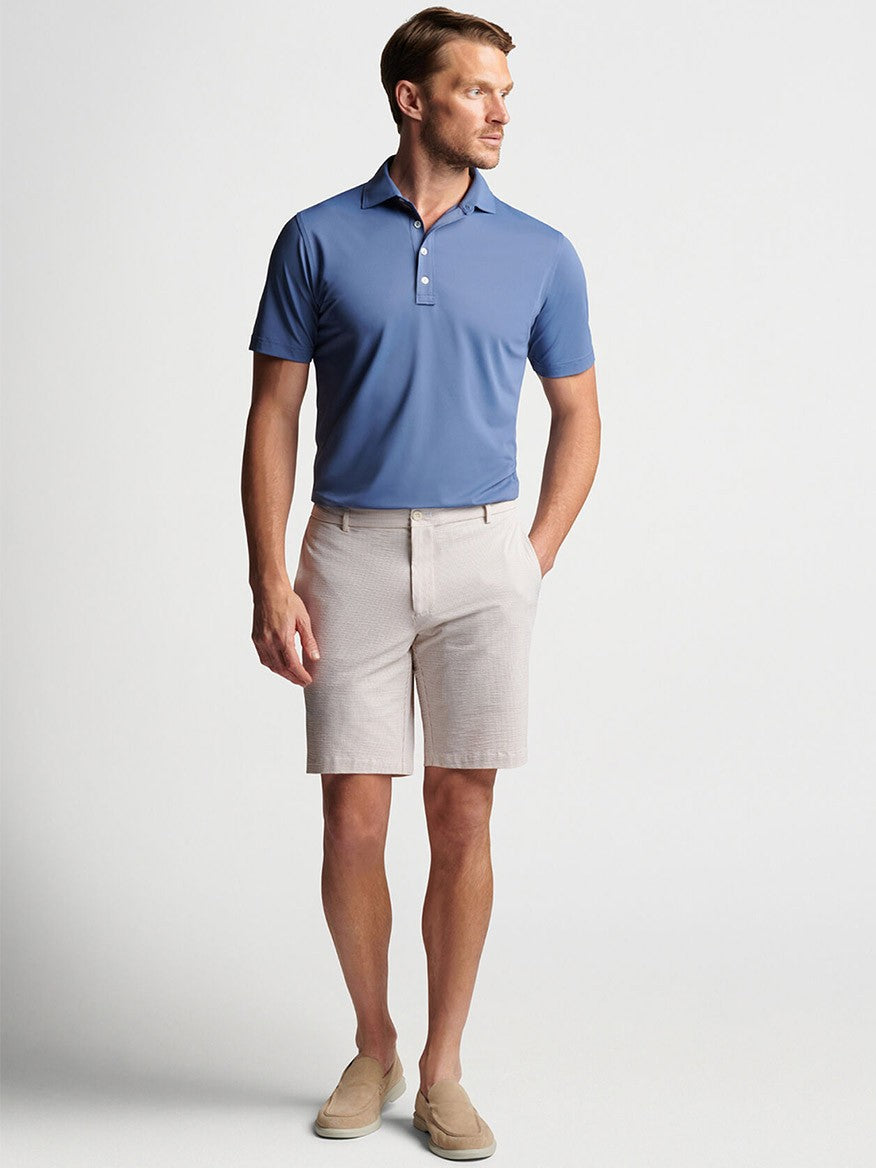 A man wearing the Peter Millar Matlock Seersucker Performance Short in Summer Dunes and a blue polo shirt, exuding warm-weather appeal.