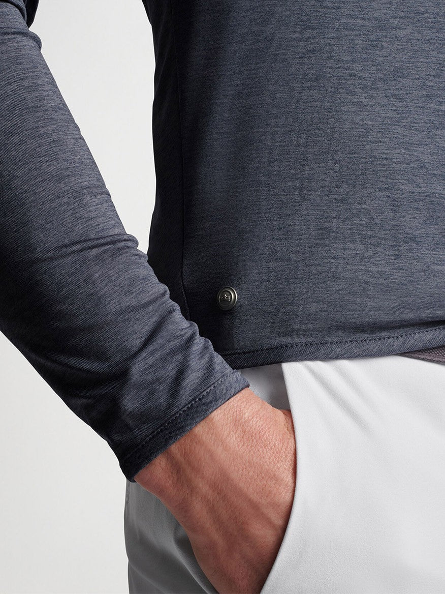Close-up of a person wearing a Peter Millar Stealth Performance Quarter-Zip in Steel with a button on the cuff, with their hand tucked into the pocket of white pants.