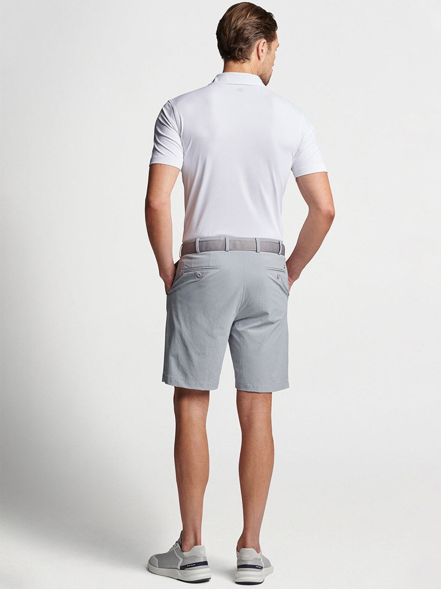 Man viewed from behind, wearing a white shirt, Peter Millar Surge Performance Short in Gale Grey, and sneakers with a belt.