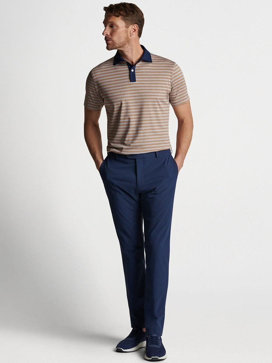 An athletic man wearing a blue and tan striped Peter Millar Surge Performance Trouser in Navy with water-resistant protection.