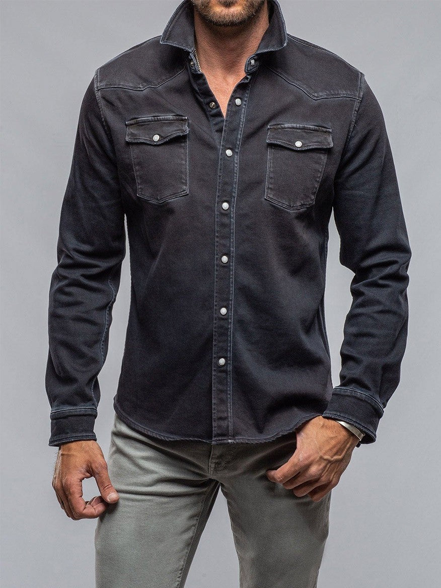 A man wearing a Teleria Zed Roper Western Snap Shirt in Nero with chest pockets, silver buttons, and gray pants stands against a plain backdrop.