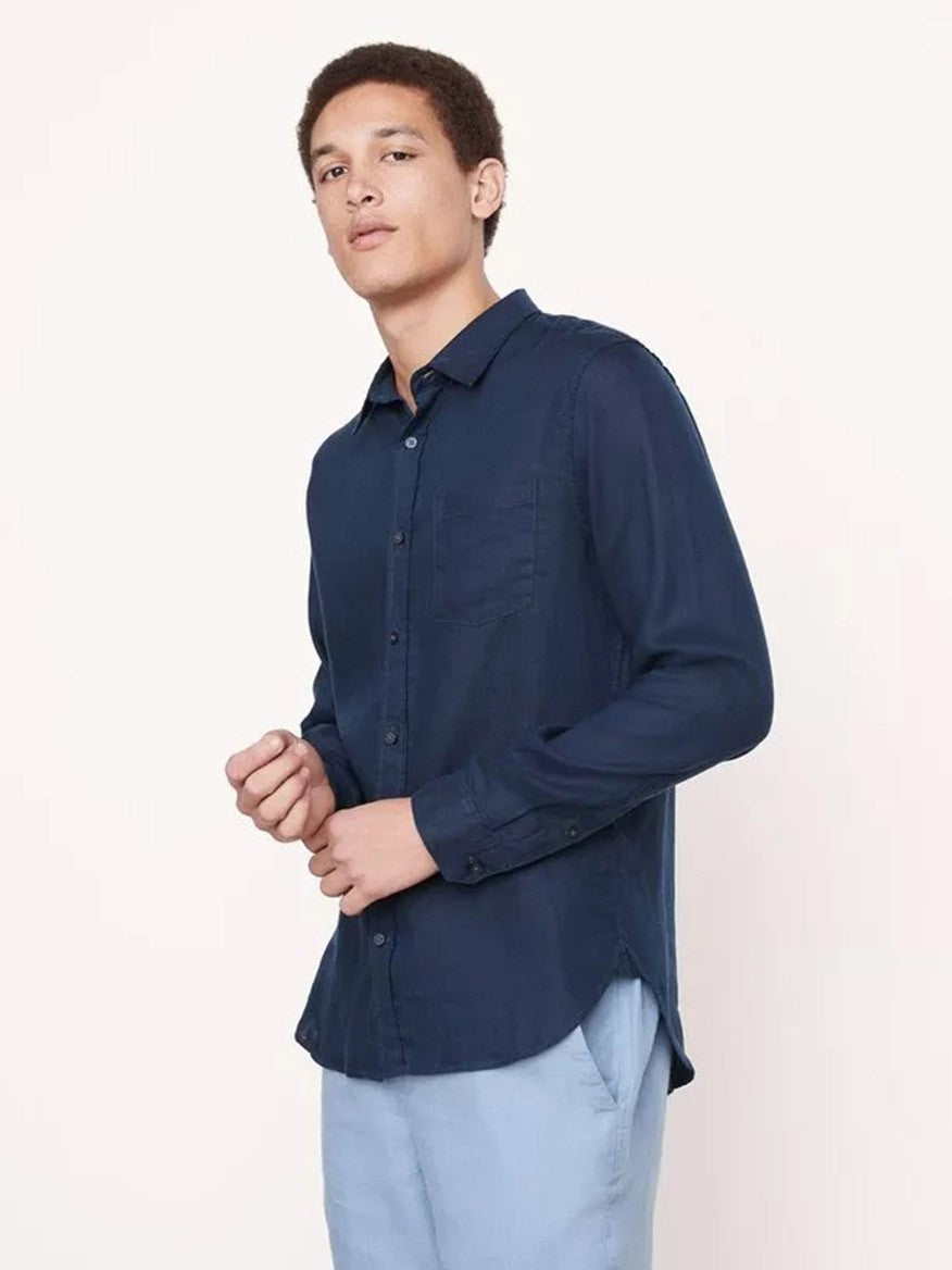 A young man wearing a Vince Linen Long Sleeve Shirt in Coastal and light blue pants stands against a light background, perfect for warm-weather.