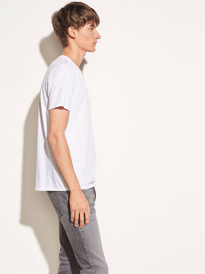 Man in Vince Crew Neck T-Shirt in Optic White and gray pants standing in profile against a light background.
