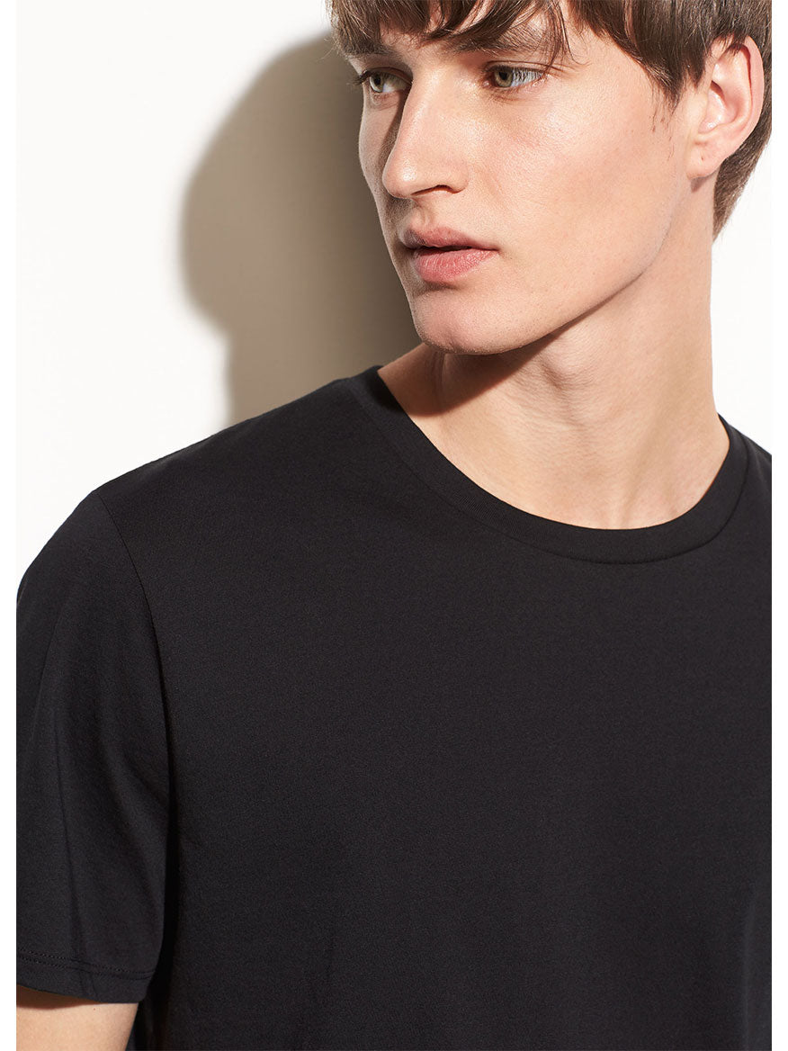 Young man in a Vince Crew Neck T-Shirt in Black with a shadow casting on a beige background.