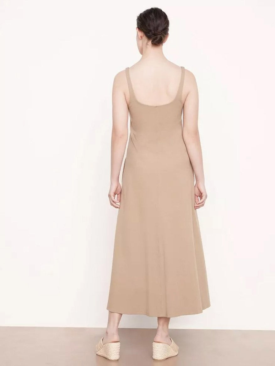 Woman in a beige slim-strapped midi Vince Paneled Trapeze Dress in Light Shale and espadrille shoes, viewed from behind, standing against a pale backdrop.