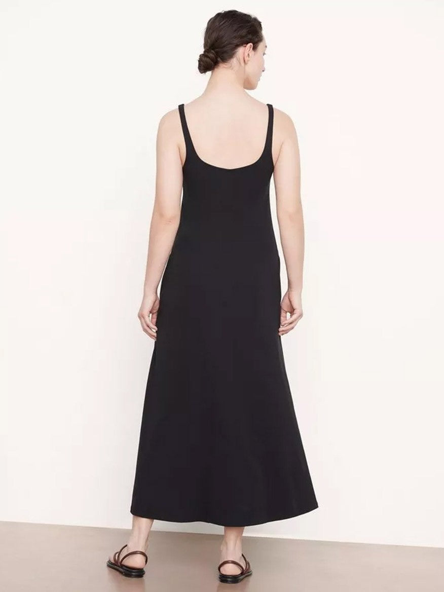 A woman wearing a long black dress viewed from the back, standing in a neutral pose against a plain background. She pairs the Vince Paneled Trapeze Dress in Black with simple black sandals.