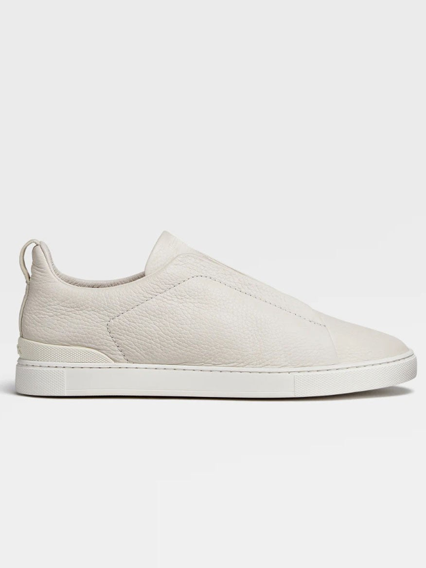 Side view of a pair of Zegna Off White Deerskin Triple Stitch™ Sneakers with a smooth texture and rubber sole, displayed against a plain background.